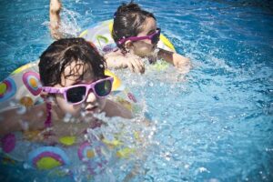 Little girls wearing colorful circular vests and goggles, having fun in a pool.